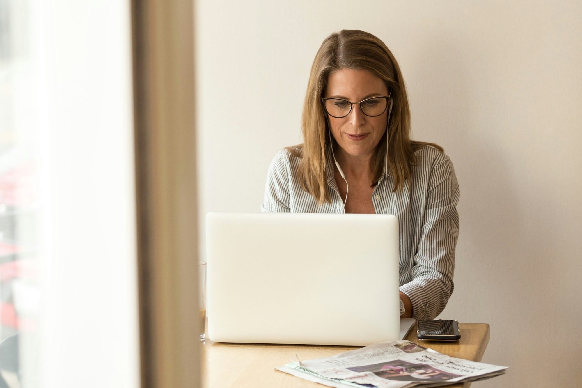 woman wearing grey striped dress shirt sitting down near brown wooden table in front of white laptop computer